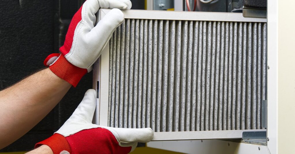 An individual in white and red gloves removing a dirty pleated air filter from a piece of equipment.