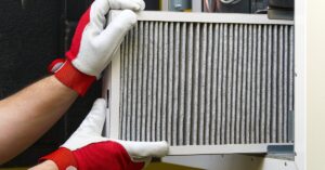An individual in white and red gloves removing a dirty pleated air filter from a piece of equipment.