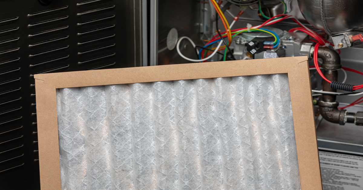 A pleated, clean air filter with a brown border sits in front of industrial machinery with pipes and wires.
