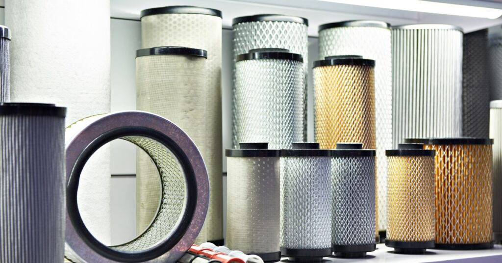 Shelves displaying cylindrical industrial air filters with pleated media, metal mesh, and rubber end caps in multiple sizes.