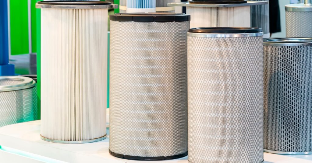 Tall cylindrical industrial air filters with pleated media and metal mesh housings displayed upright on a white surface.