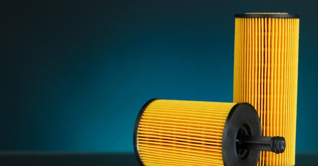 Two yellow pleated cylindrical air filters, one upright and one lying down, against a dark teal background.