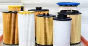 Multiple cylindrical industrial air filters with pleated paper media arranged on a metal surface in a workshop setting.